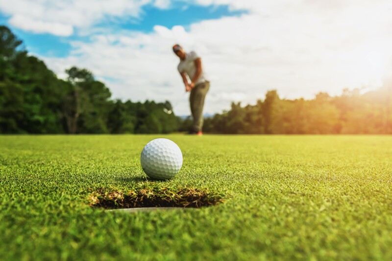 A golf ball just ahead of a hole with a golfer in the far distance. Strategies to hit a better short approach shot in golf.